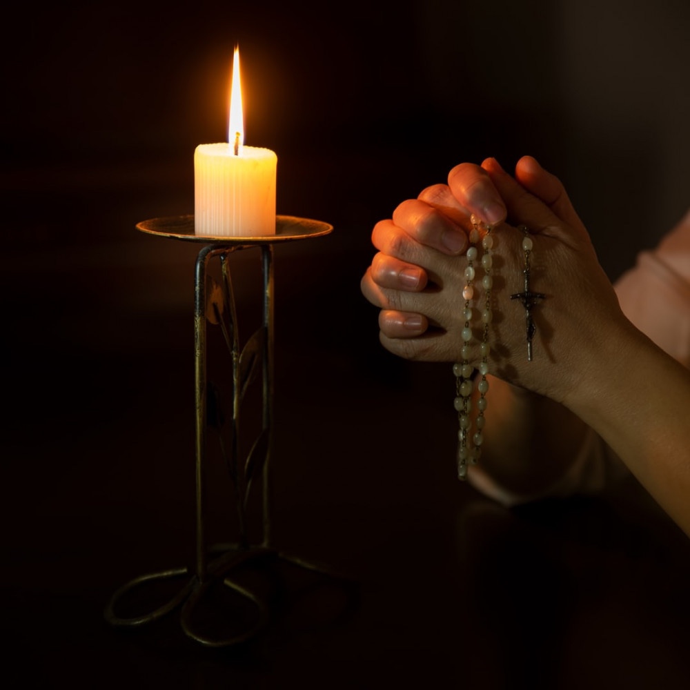 Praying with a rosary next to a candle in the dark