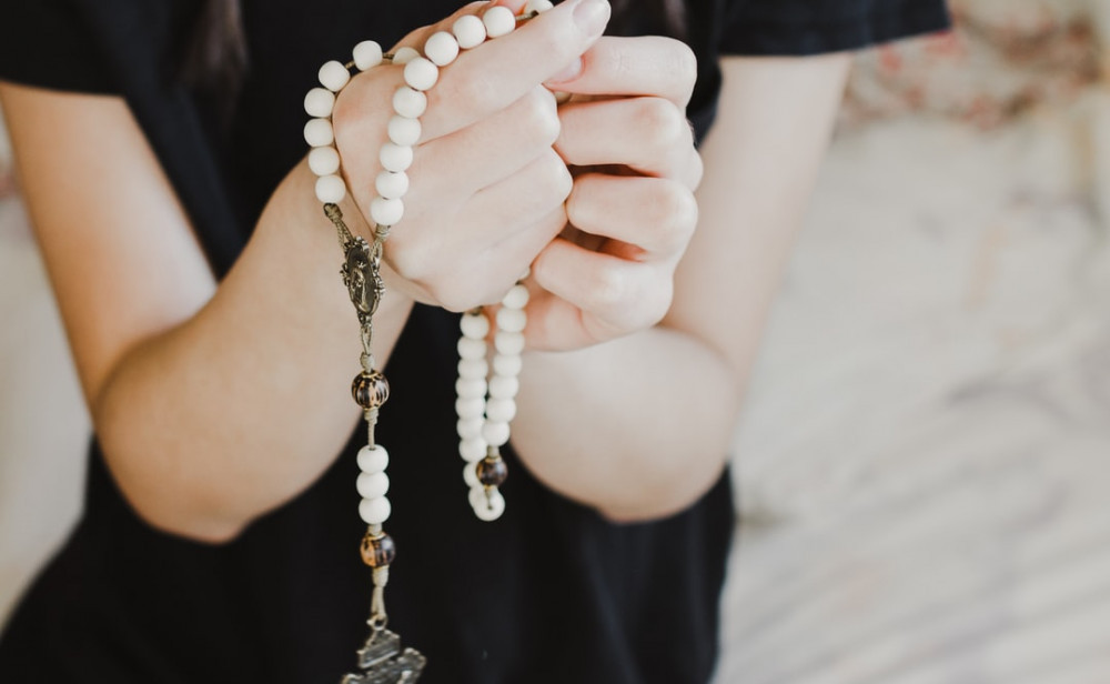 A woman's hands clutching a rosary made of white stones