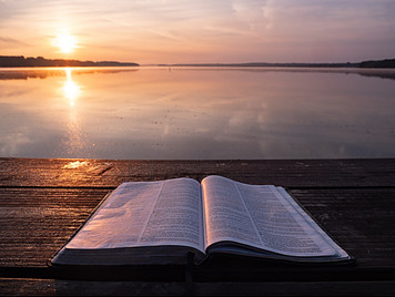 A Bible laid out before the sun and sea at sunset