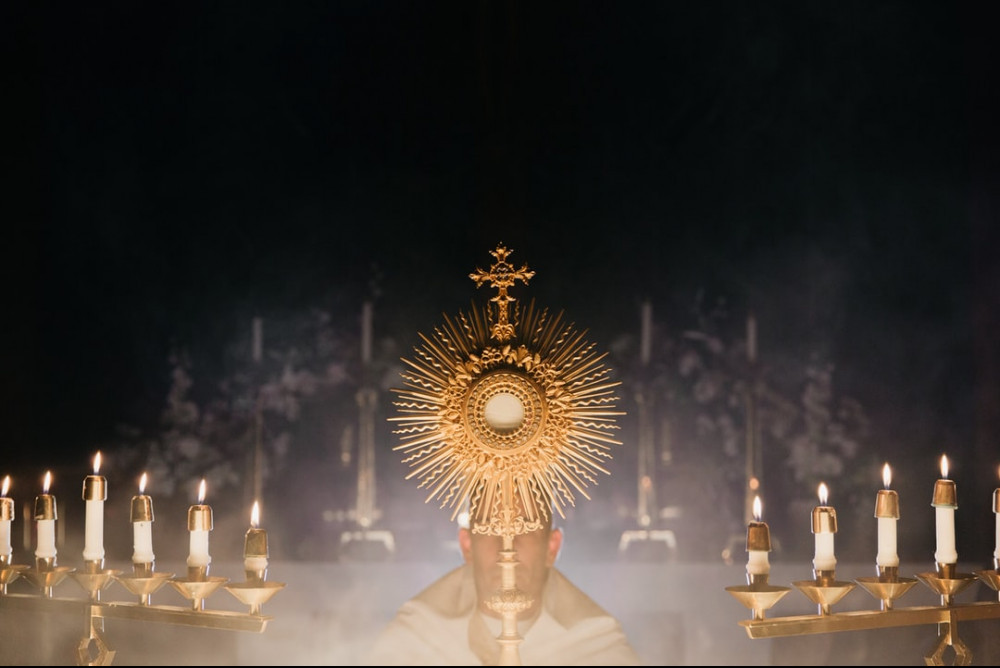 A priest holding up the Blessed Sacrament amongst candles; beautiful picture