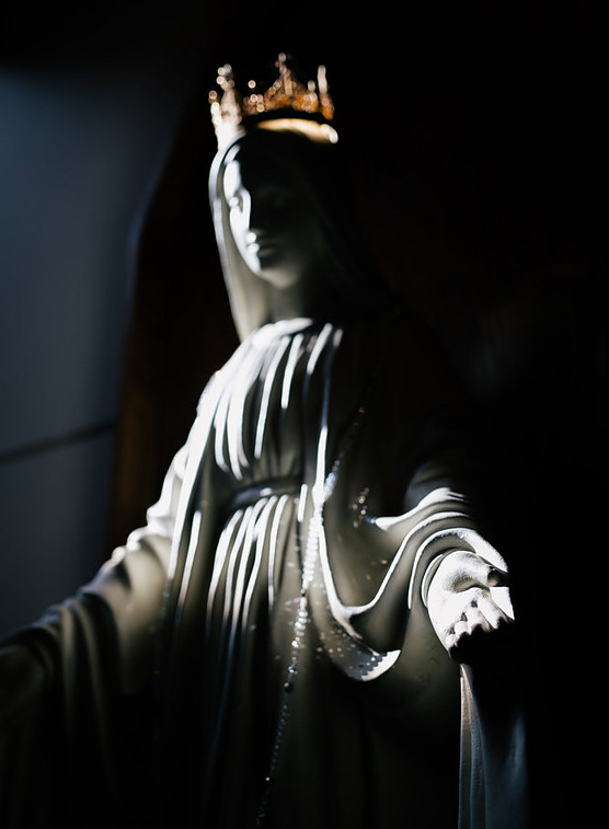 A statue of Mary, crowned with a gold crown, with a very dark backdrop