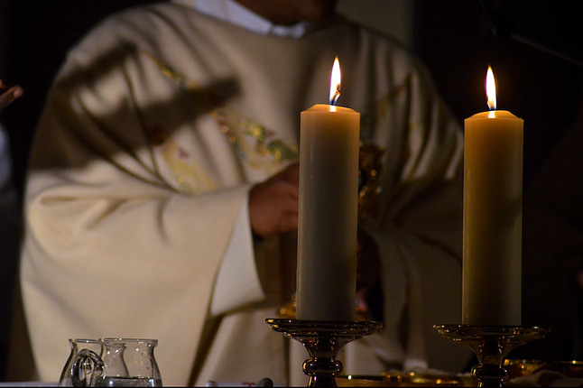 A Catholic priest in low lighting before two candles
