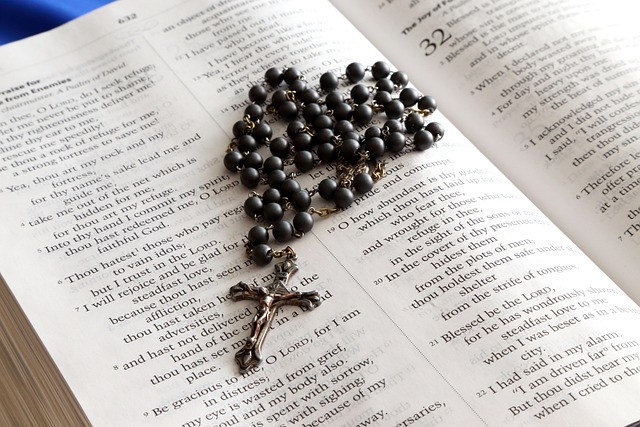 A set of rosary beads with black beads resting on a Bible